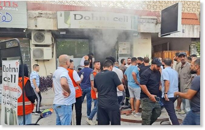 People gather as smoke rises from a mobile shop in Sidon, Lebanon