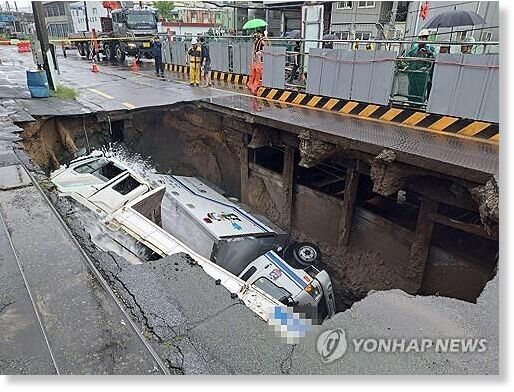 Click to enlarge Trucks remain overturned inside a sinkhole on a road in the southeastern city of Busan on Sept. 21, 2024, following heavy rainfall, in this photo provided by fire authorities.
