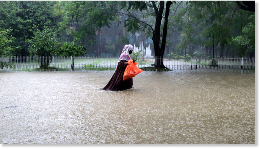 A woman wades through knee-deep water during heavy rainfall in Sylhet city.