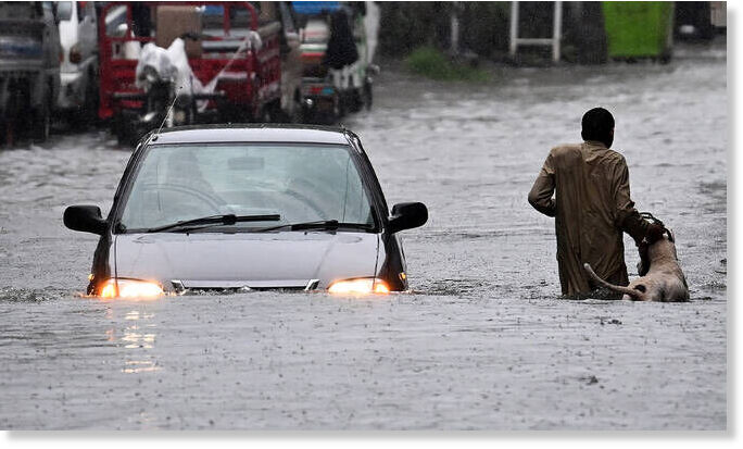 Click to enlarge A man along with his dog while a car wade through a flooded street during heavy monsoon rains in Rawalpindi on July 17, 2025.