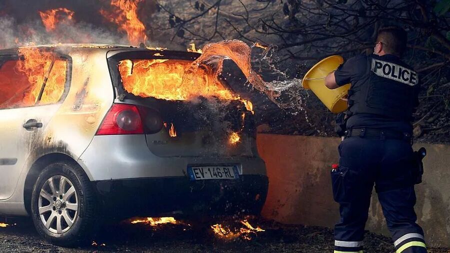 Click to enlarge A police officer tries to put out a fire in a car near Marseille