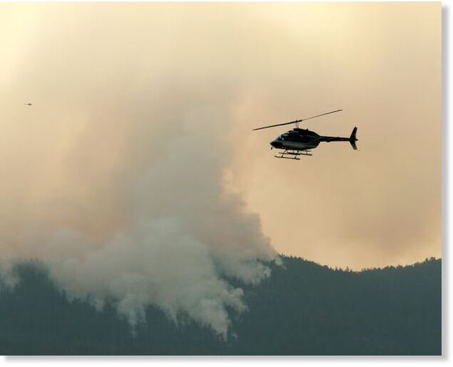Click to enlarge A helicopter flies by the Wesley Ridge wildfire near Coombs, British Columbia, on Sunday.