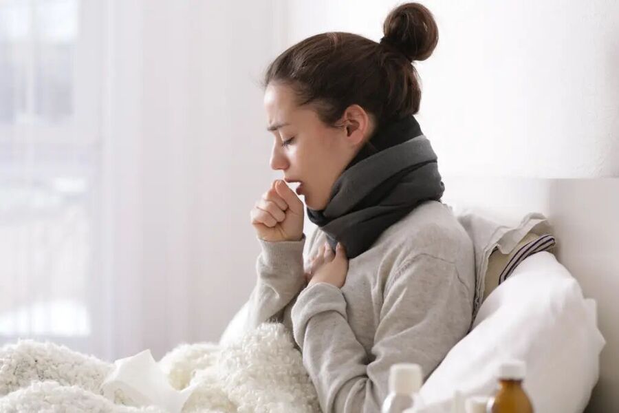 Young woman coughing in bed, appearing ill