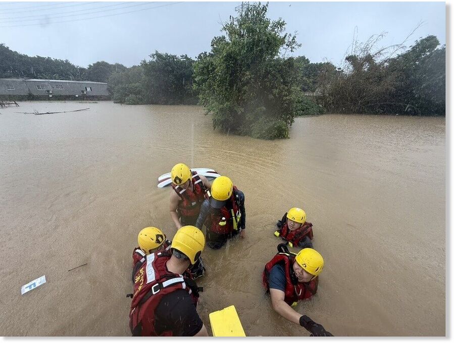 Hsinchu County rescue workers wade through floodwaters in Zhubei on Friday during search operations for a vehicle stranded by flooding.