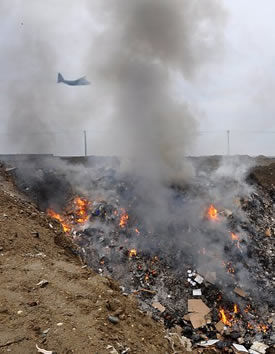 A C-130 Hercules transport plane flies through a tower of smoke caused by open burning in a trash pit at Bagram Airfield.