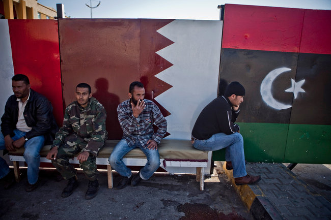 Click to enlarge Libyans in Benghazi last year in front of a Libyan flag, right, and a Qatari flag painted on the wall.