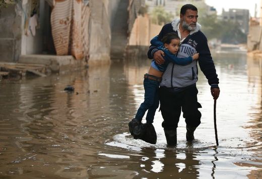 Palestinian man holds a boy on a street flooded with sewage water in Gaza City
