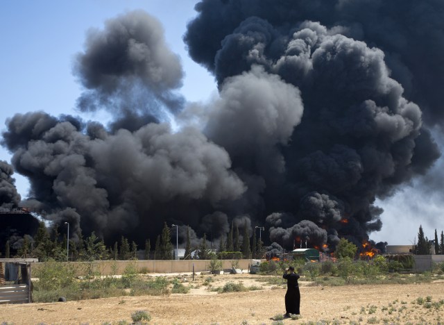 Click to enlarge Palestinian man stands looking as fuel tanks burn